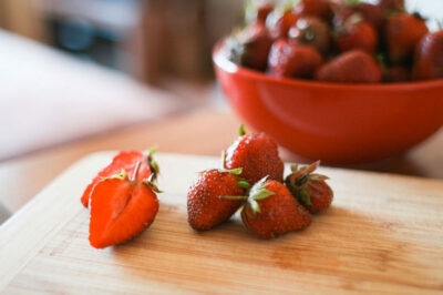 A bowl of strawberries and some cut up strawberries.