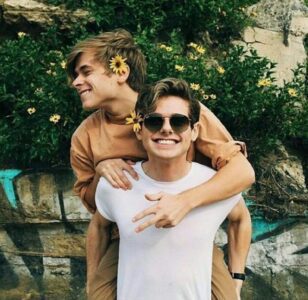 Here's a short alt tag for the image: Two smiling young men hugging outdoors.