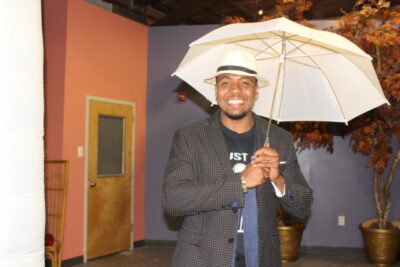 A man holding an umbrella while wearing a hat.