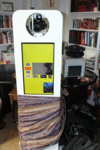 A photo booth with a yellow screen and purple skirt.