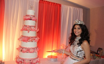 A woman in a tiara standing next to a cake.