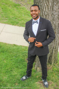 A man in a suit and bow tie standing next to a tree.