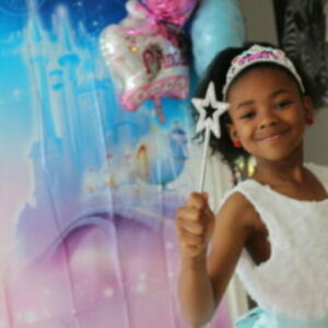 A little girl holding a star wand in front of balloons.