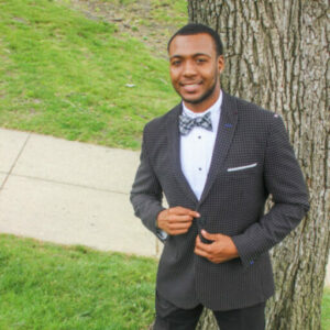 A man in a suit and bow tie standing next to a tree.