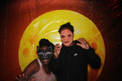 A man and woman posing for a picture in front of an orange background.
