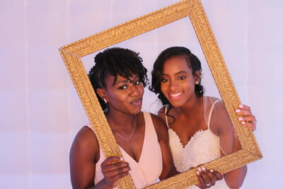 Two women posing for a picture in a gold frame.