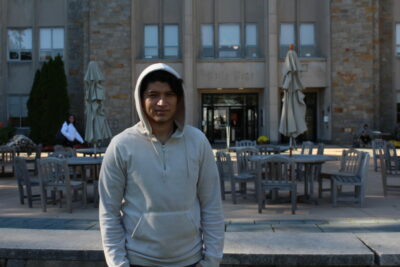 A man in a gray hoodie stands outside of an outdoor restaurant.