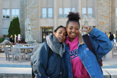 Two young women posing for a picture outside of a building.
