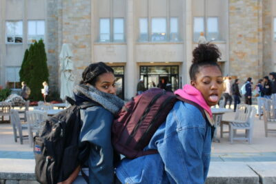 Two young women are walking on the sidewalk.