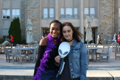 Two young women posing for a picture with an alien mask.