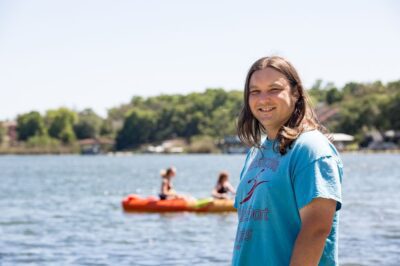Smiling woman by lake with kayakers.
